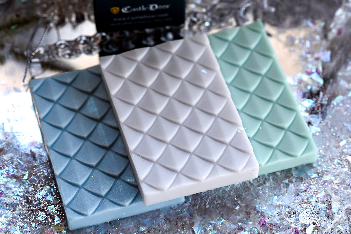 Blue, white, and pale green dragonscale wax melt snap bars from Castle Door's Eternal Winter Trilogy, displayed on a frosty surface.